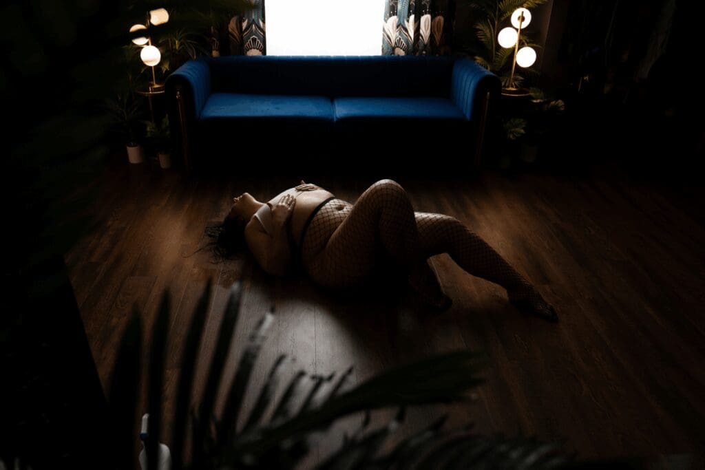 Woman lying on studio floor in fishnet stockings during a moody wet set boudoir session in Sioux Falls, South Dakota