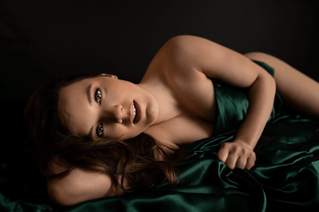 Woman wrapped in emerald satin lying on a bed during a boudoir session in Sioux Falls, South Dakota