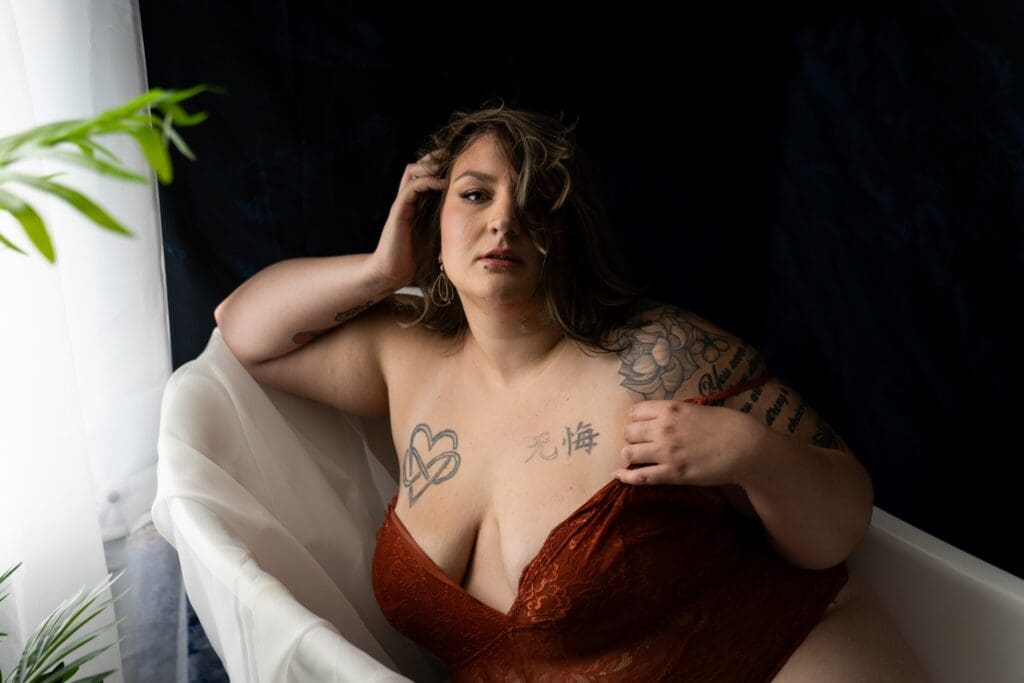 Woman in rust lace lingerie posing in a clawfoot bathtub during a boudoir session in Sioux Falls, South Dakota